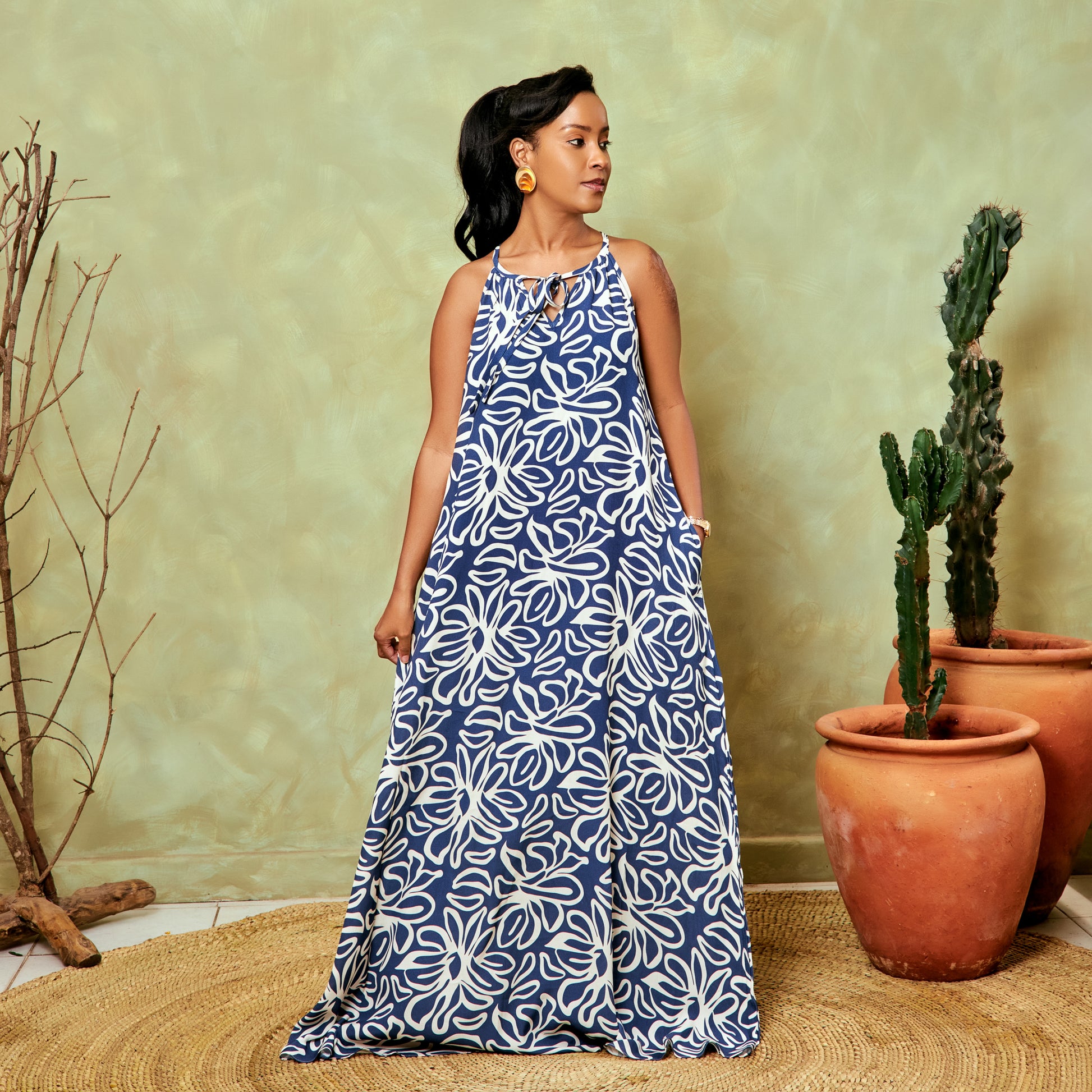 Woman wearing a blue and white patterned dress standing in front of potted plants.
